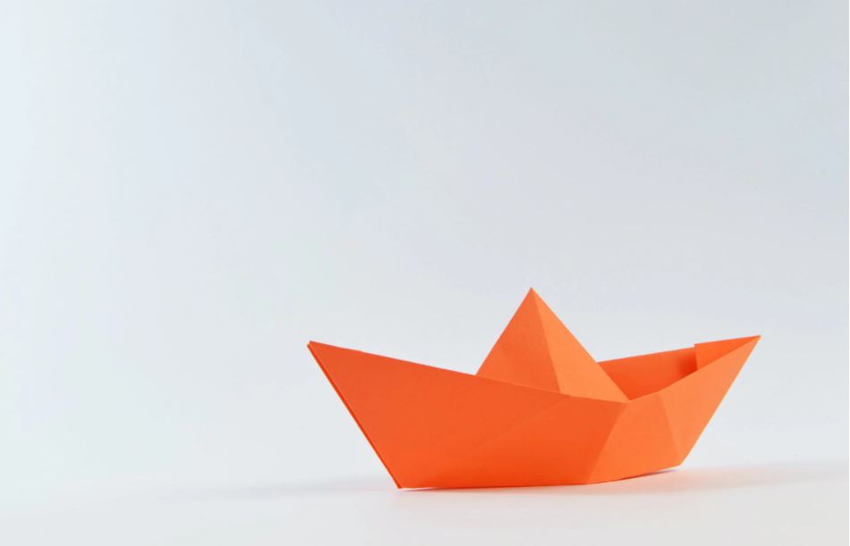 An orange origami boat against a white background